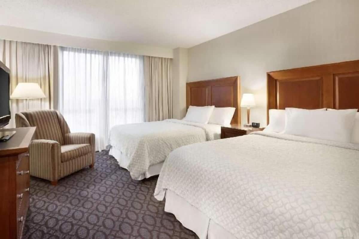 Habitación de hotel con dos camas, un escritorio, una silla y un televisor.