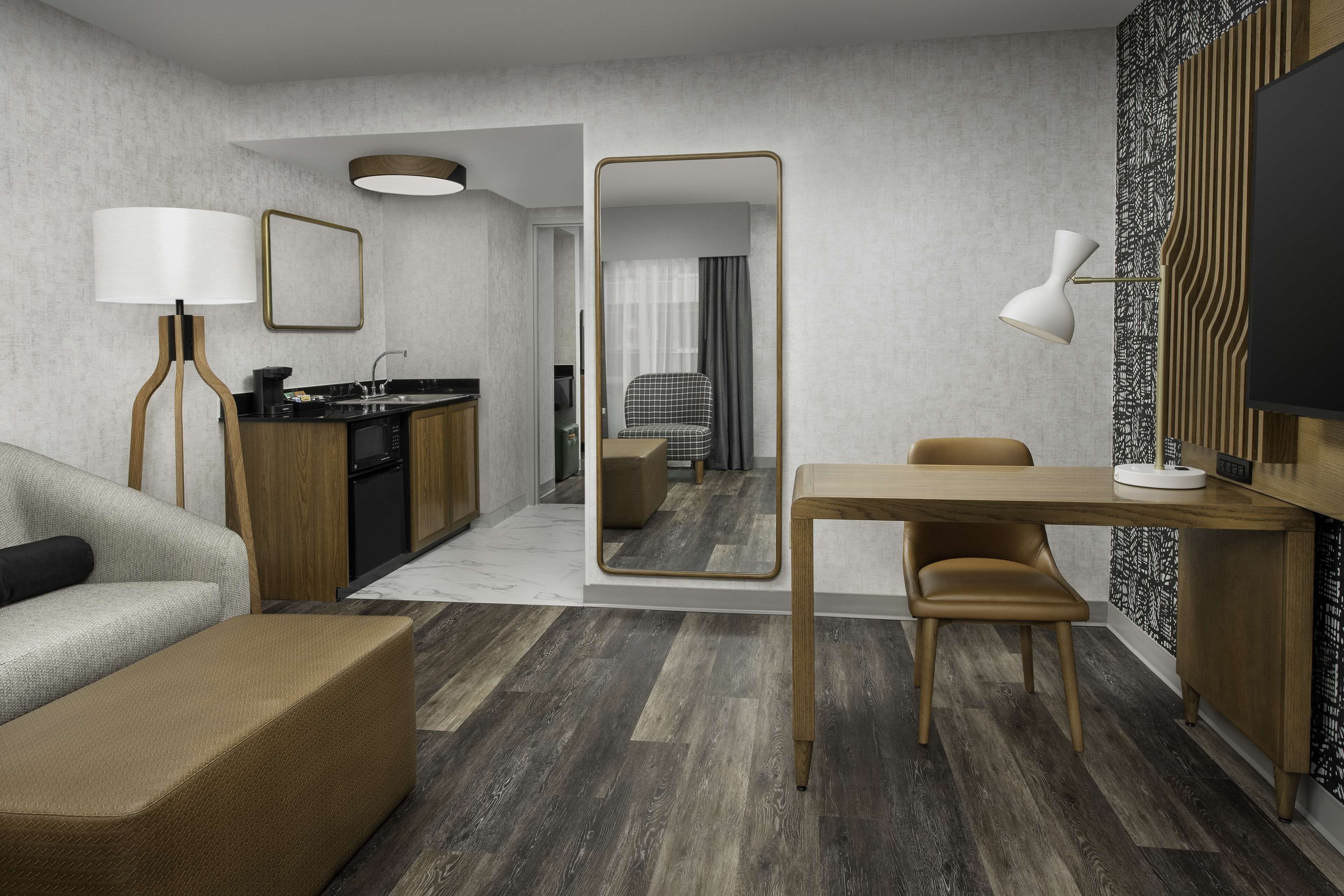 Quarto de hotel moderno com sofá, mesa de jantar de madeira, TV e cozinha.