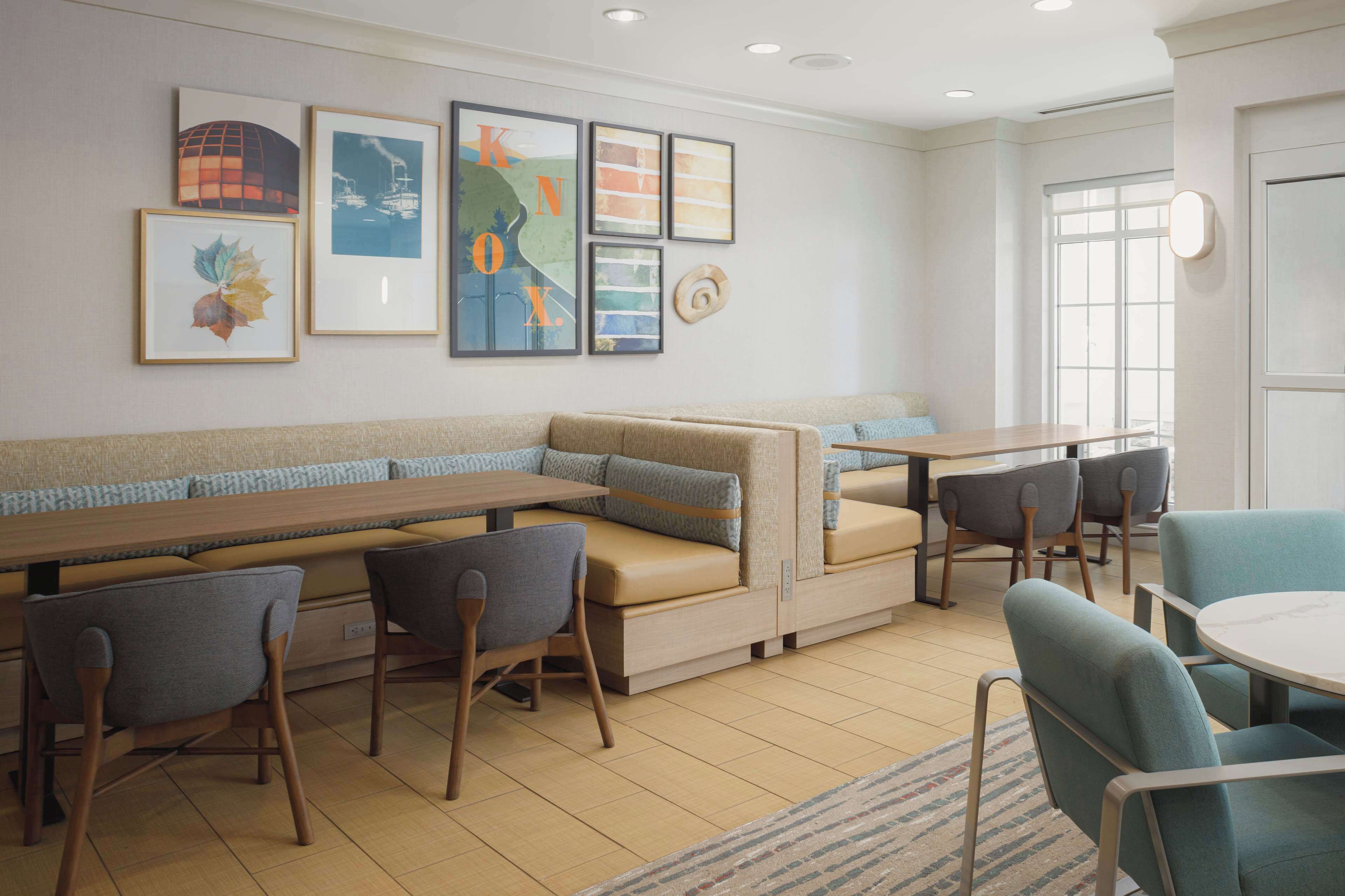 A modern dining area with a long wooden table, cushioned seating, and framed artwork on the walls.