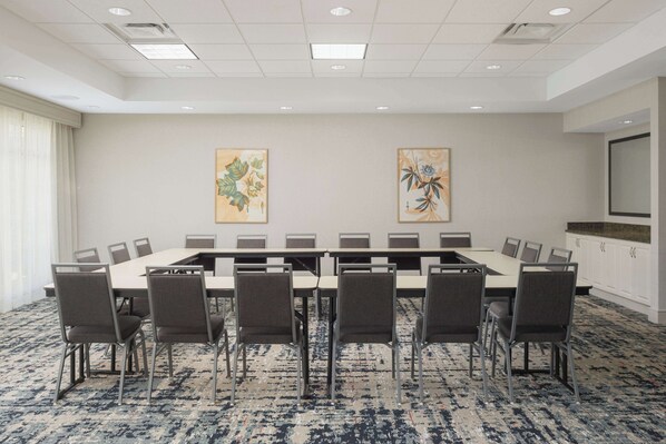 A conference room with a long table, six chairs, and two large paintings on the wall.