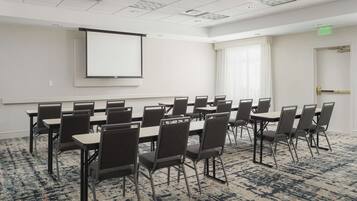 A conference room with a projector screen, multiple tables, and chairs.