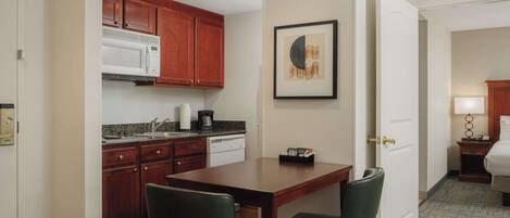 A compact hotel room with a kitchenette, a dining area, and a bed.