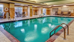 An indoor swimming pool with a lifeguard chair, lounge chairs, and a table with chairs.