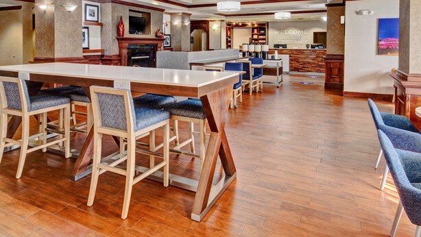 A spacious hotel lobby with a central bar area, seating arrangements, and a reception desk.
