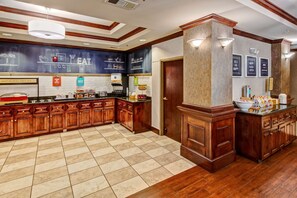 A hotel kitchen with wooden cabinets, a tiled floor, and a chalkboard menu.
