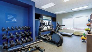 A gym with exercise equipment, a wall-mounted clock, and a window with blinds.