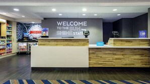 A reception area with a 'Welcome to the Sun Shine Station' sign, a self-service kiosk, and a 'Treats' section with snacks. - Hampton Inn & Suites Tallahassee I-10/Thomasville Road, FL (Tallahassee)