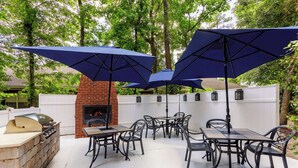An outdoor patio with a brick fireplace, metal tables and chairs, and large umbrellas. - Hampton Inn & Suites Tallahassee I-10/Thomasville Road, FL (Tallahassee)