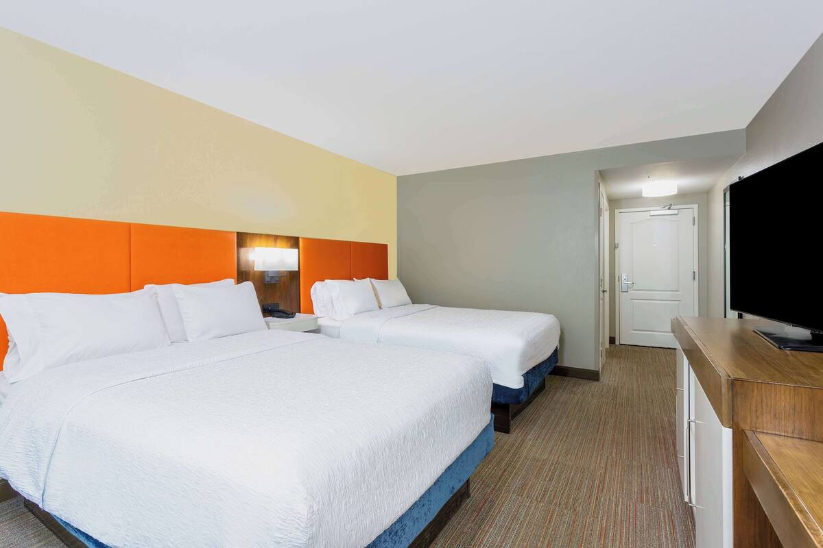 A hotel room with two beds, a TV, and a desk.