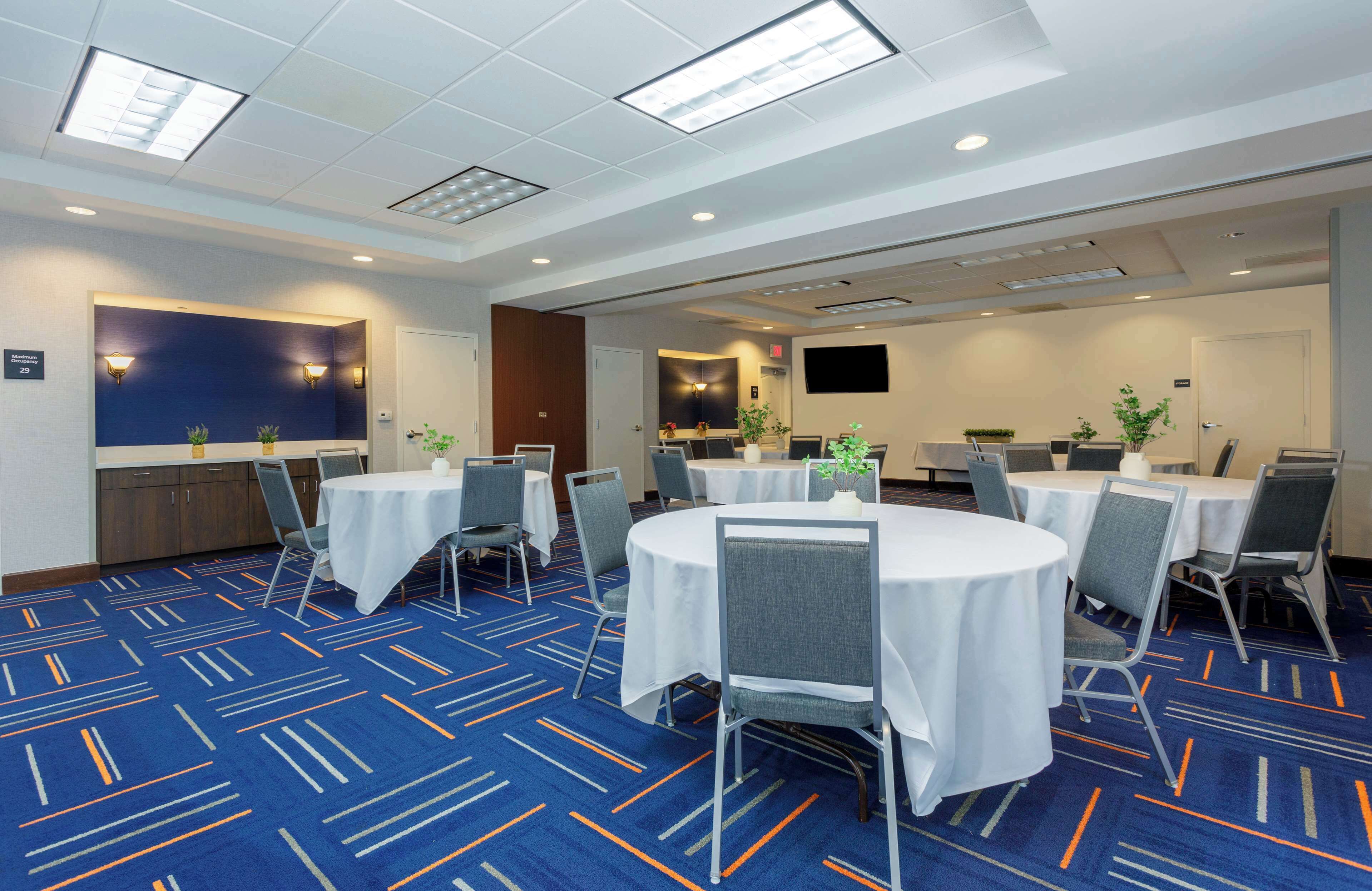 A conference room with round tables, chairs, and a blue carpet with white and orange lines.