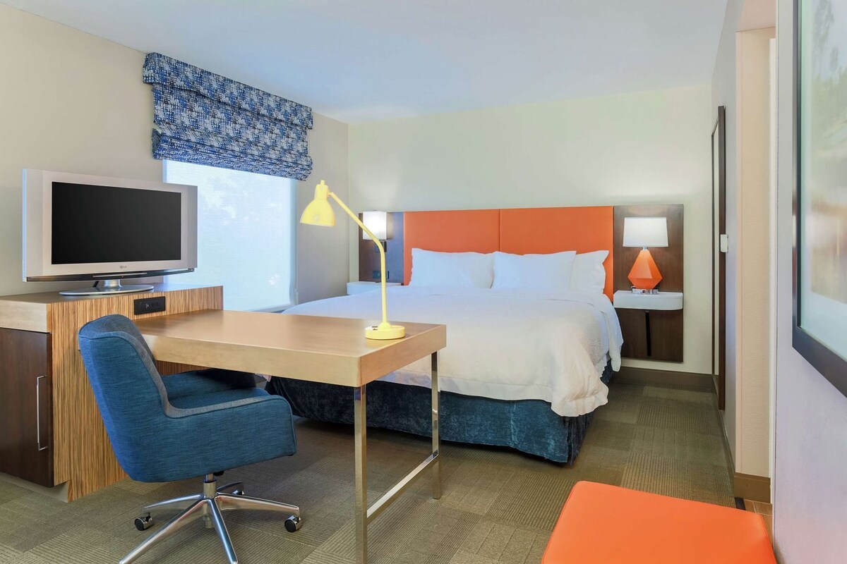 A hotel room with a bed, desk, chair, television, and two bedside lamps.