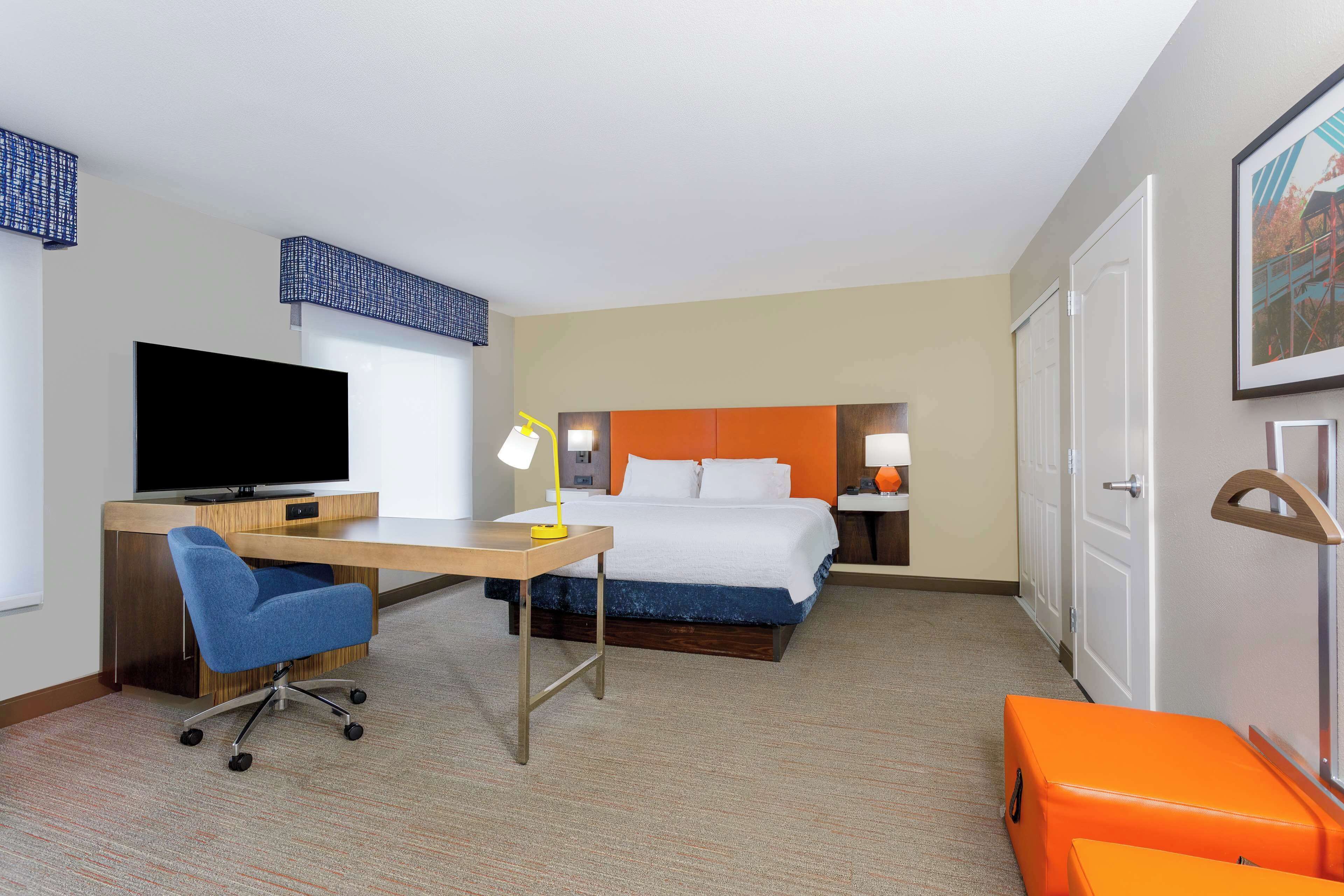 Una habitación de hotel con cama, escritorio, silla, televisión y maleta.