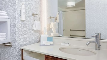 A modern bathroom with a white sink, a large mirror, and a towel rack.