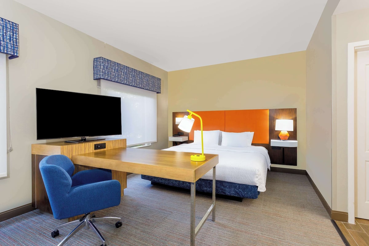 A hotel room with a bed, a desk with a chair, a television, and a lamp.