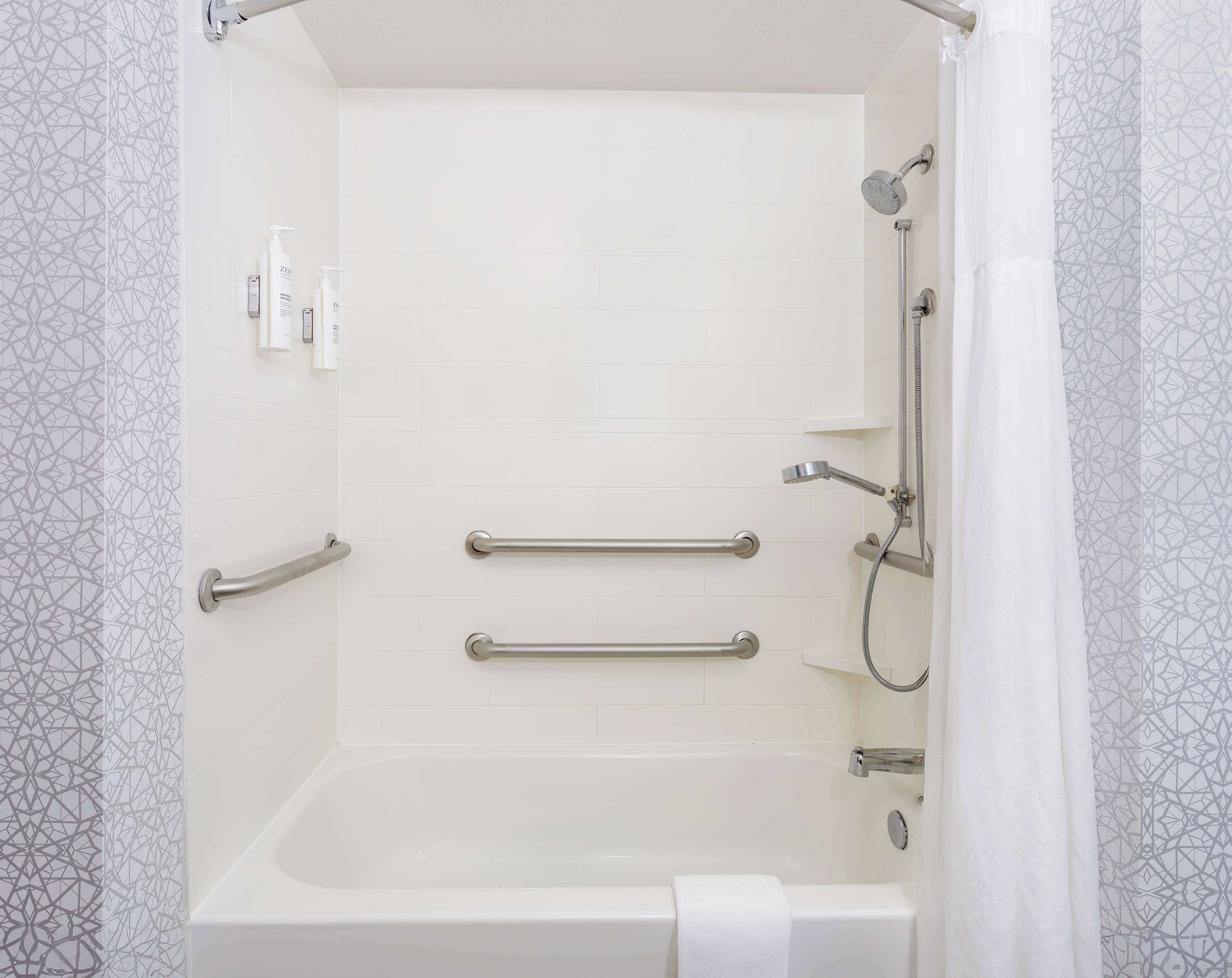 Eine begehbare Dusche mit Badewanne, Haltegriffen und Duschbrause.