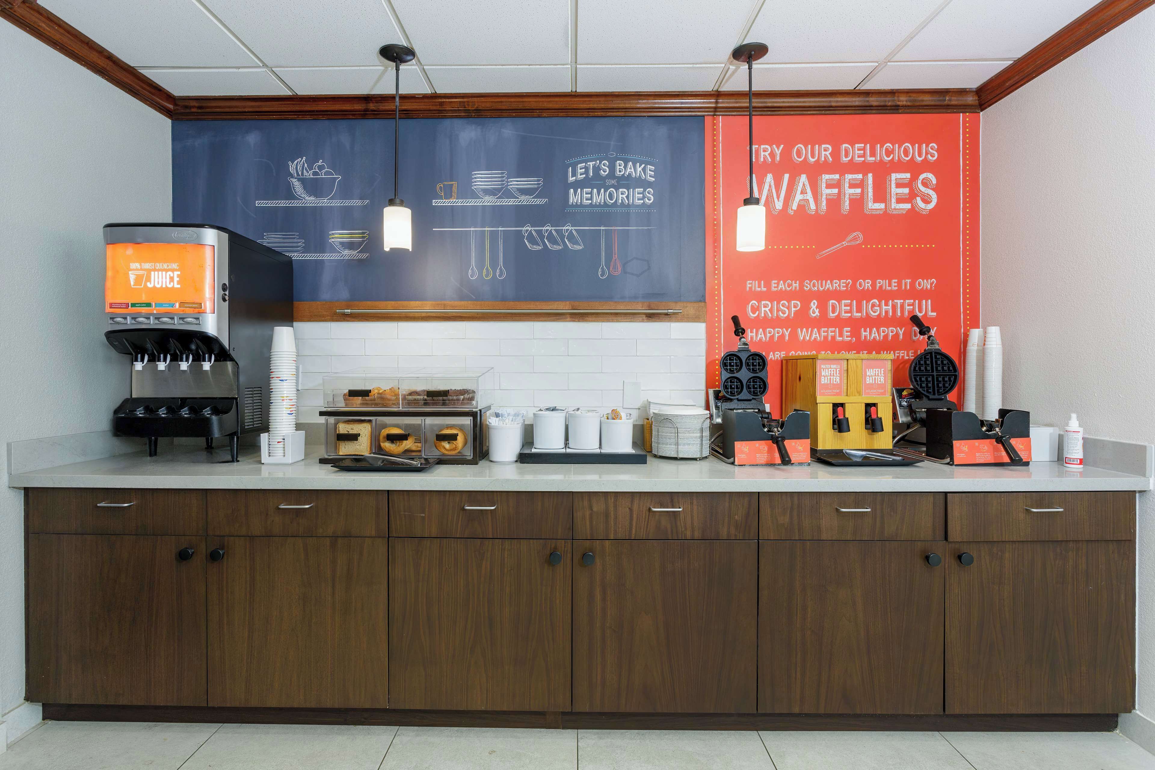 A kitchen counter with a juice dispenser, waffle maker, and waffle display.