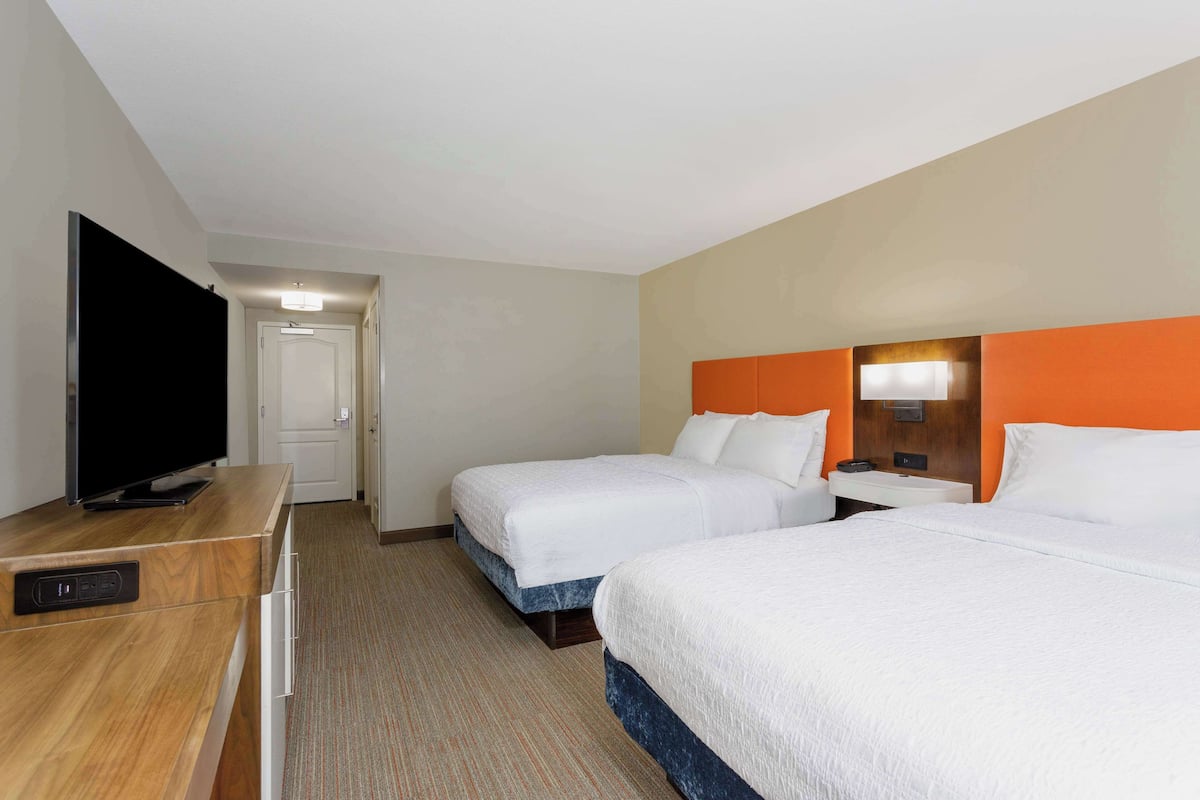 A hotel room with two beds, a TV, a desk, and a door leading to another room.
