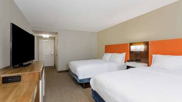 Habitación de hotel con dos camas, un televisor, un escritorio y una puerta que da a otra habitación.