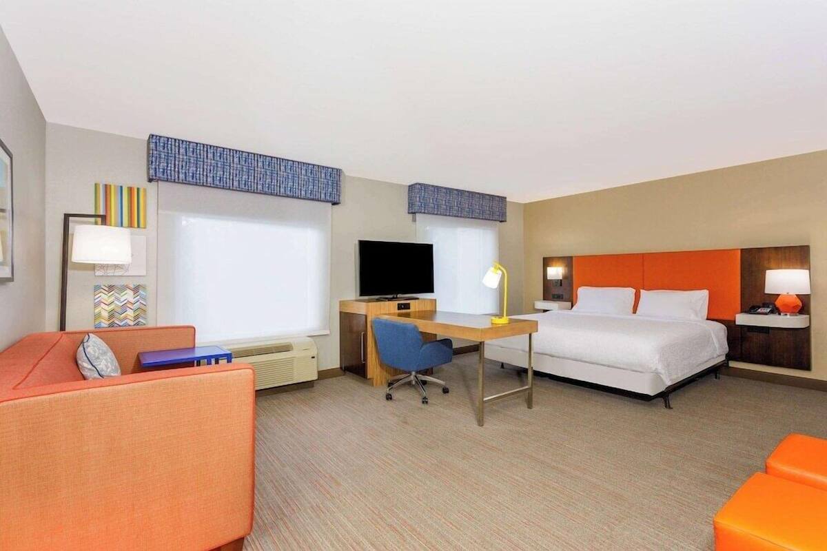 A hotel room with a bed, desk, chair, and a sofa.