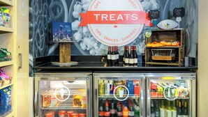 A beverage cooler with various drinks and snacks, a sign indicating treats available, and a mural in the background. - Hampton Inn & Suites Tallahassee I-10/Thomasville Road, FL (Tallahassee)