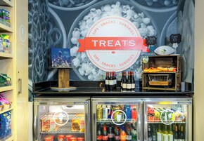 Un refrigerador con diversas bebidas y aperitivos, un cartel que indica dulces disponibles y un mural de fondo.