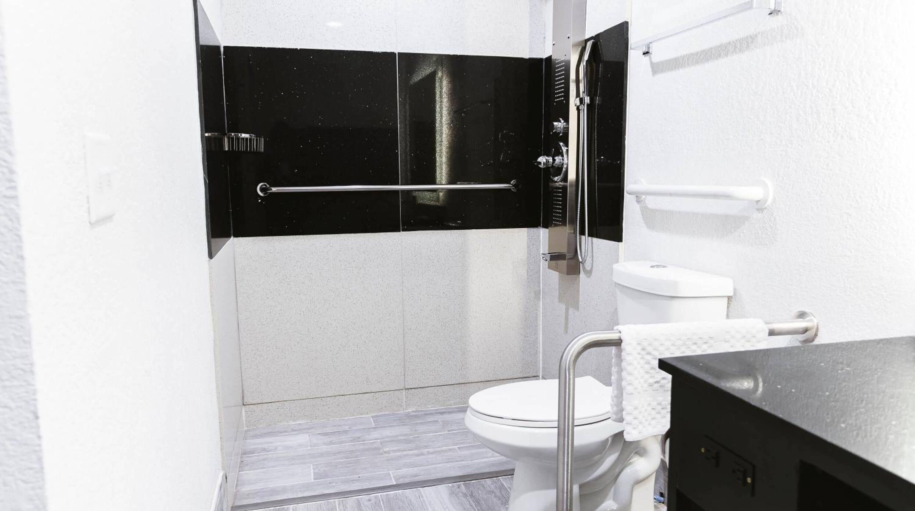 Ein modernes Badezimmer mit Toilette in Weiß, einer schwarzen Duschkabine und einem weißen Waschbecken mit Handtuch.