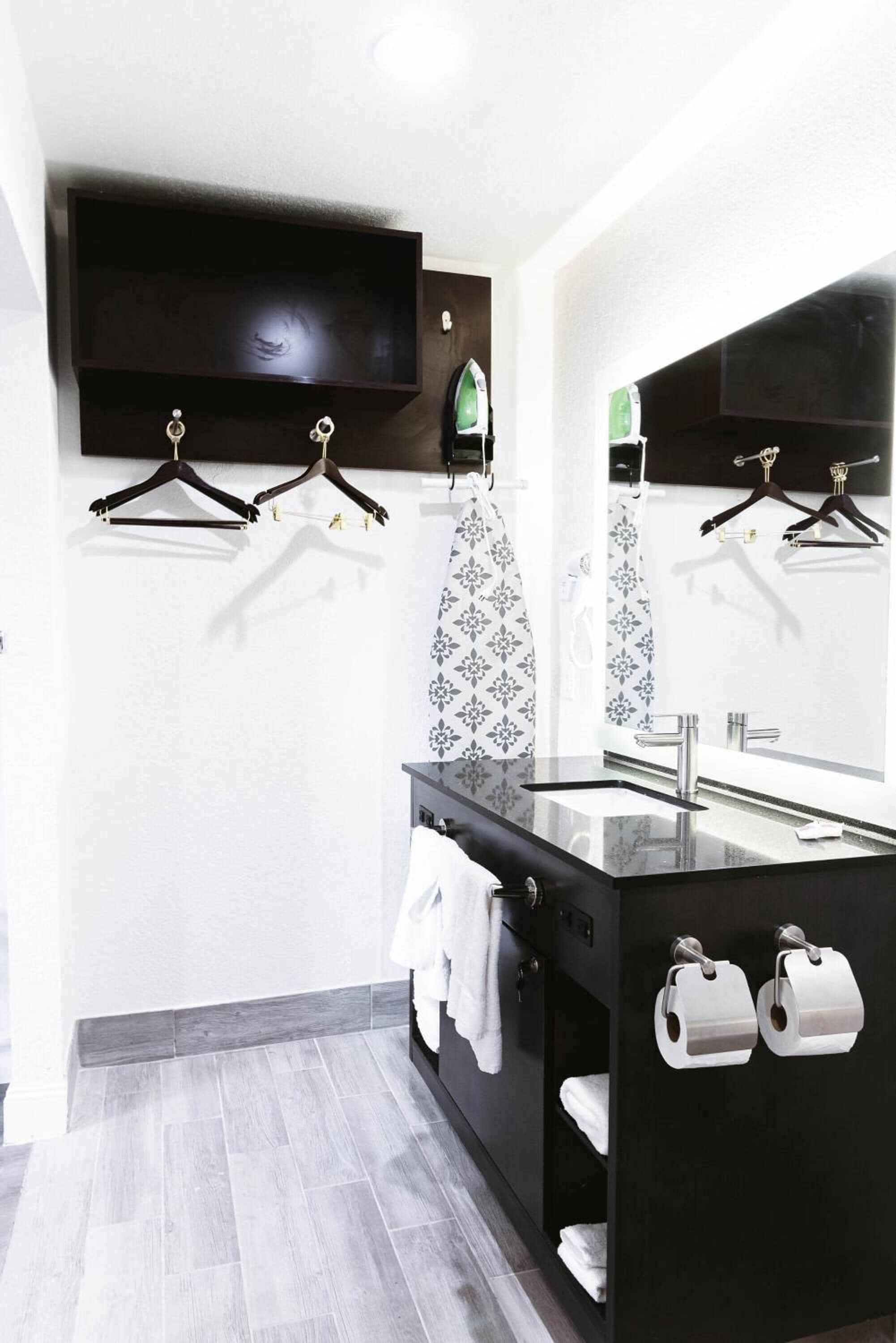 A modern bathroom with a black vanity, a large mirror, and two towel racks.