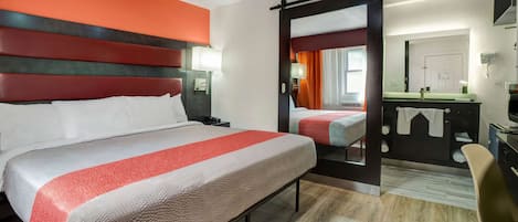 A hotel room with a large bed, a desk, a chair, and a bathroom visible through an open door.