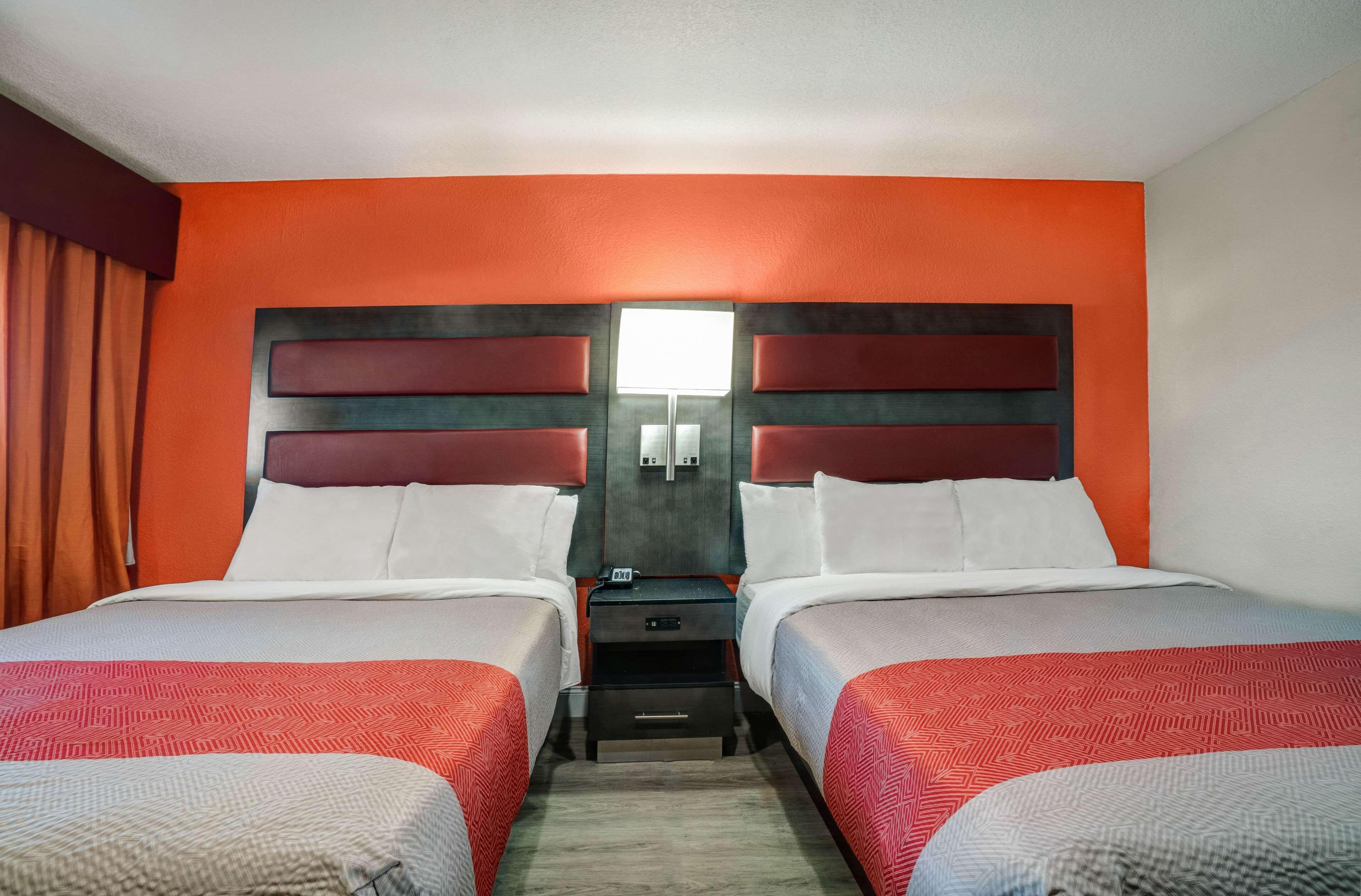 Habitación de hotel con dos camas, una mesita de noche y una lámpara de pared.