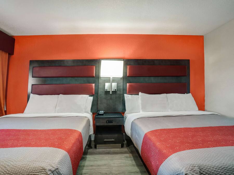 Habitación de hotel con dos camas, una mesita de noche y una lámpara de pared.