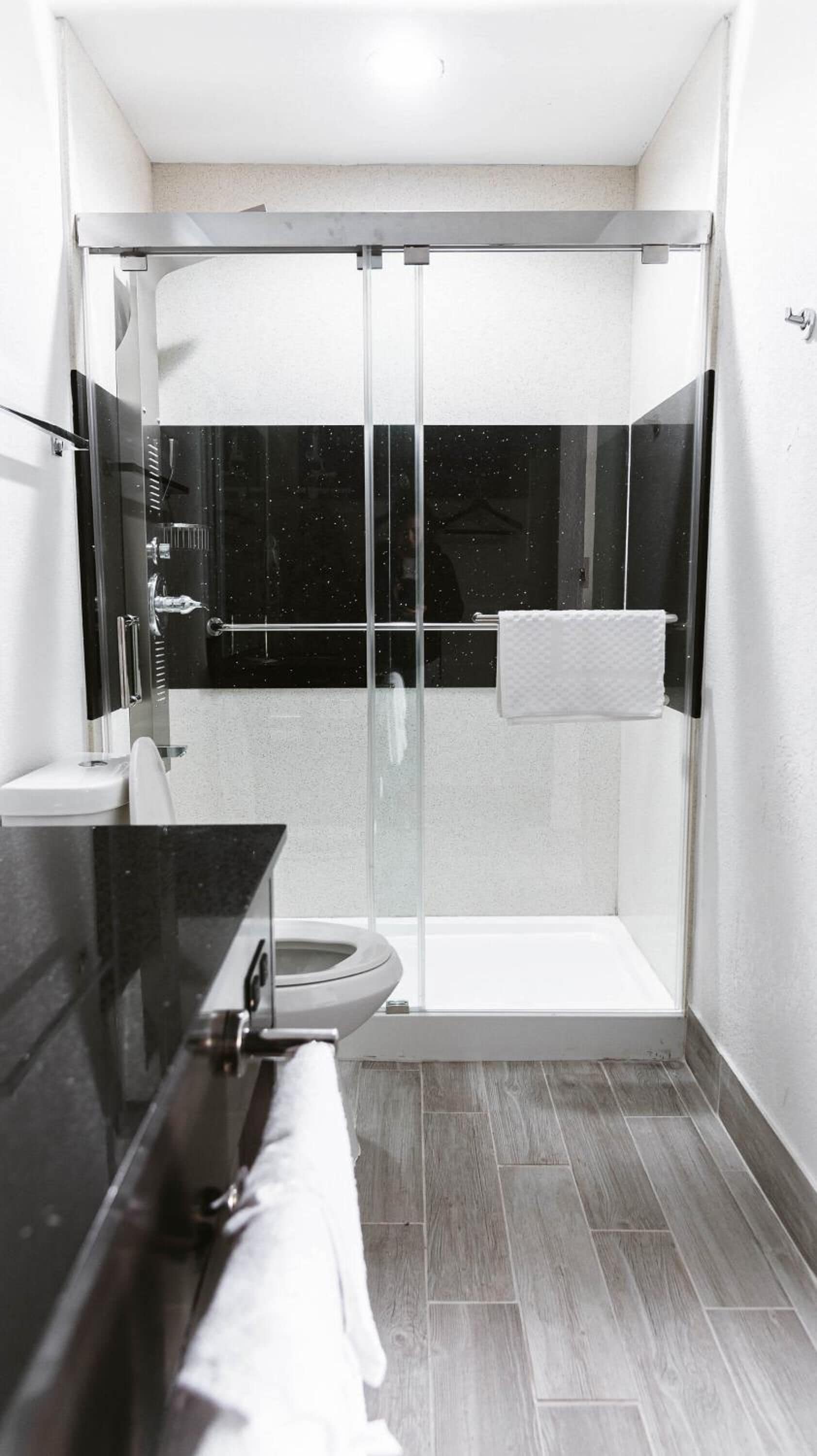 A modern bathroom with a glass-enclosed shower, a toilet, and a sink with a towel rack.