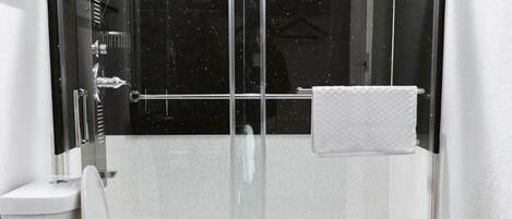 A modern bathroom with a glass-enclosed shower, a toilet, and a sink with a towel rack.