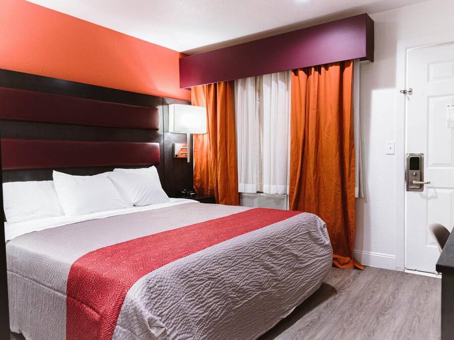 Hotellihuone, jossa on suuri sänky, sängynpääty, yöpöytä, lamppu ja ovi.