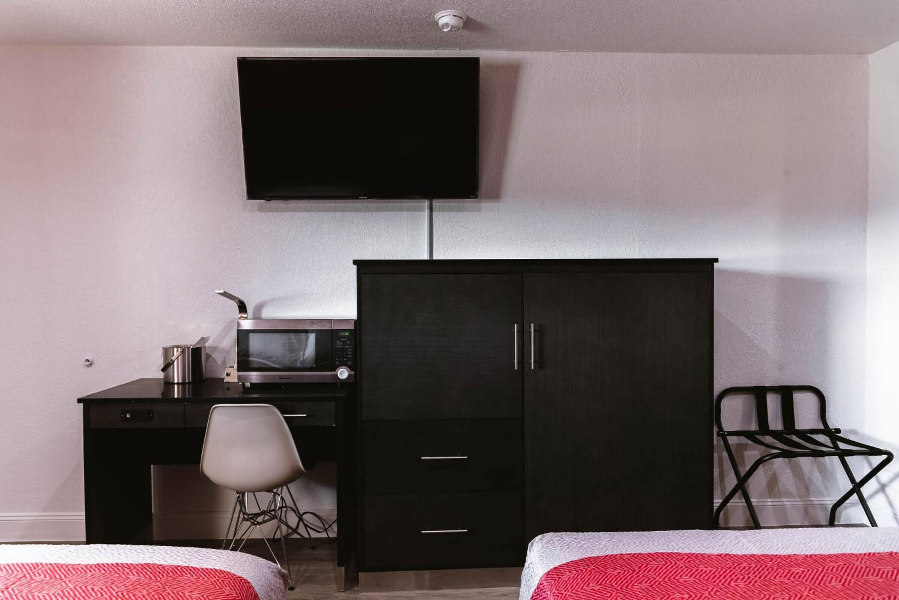 Habitación de hotel con cama, escritorio con microondas, televisor y armario.