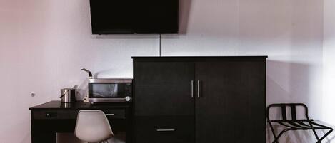 A hotel room with a bed, a desk with a microwave, a TV, and a wardrobe.