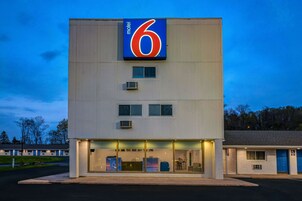 Un motel con un llamativo letrero con el número '6', varias habitaciones y una zona de servicio con acceso vehicular.