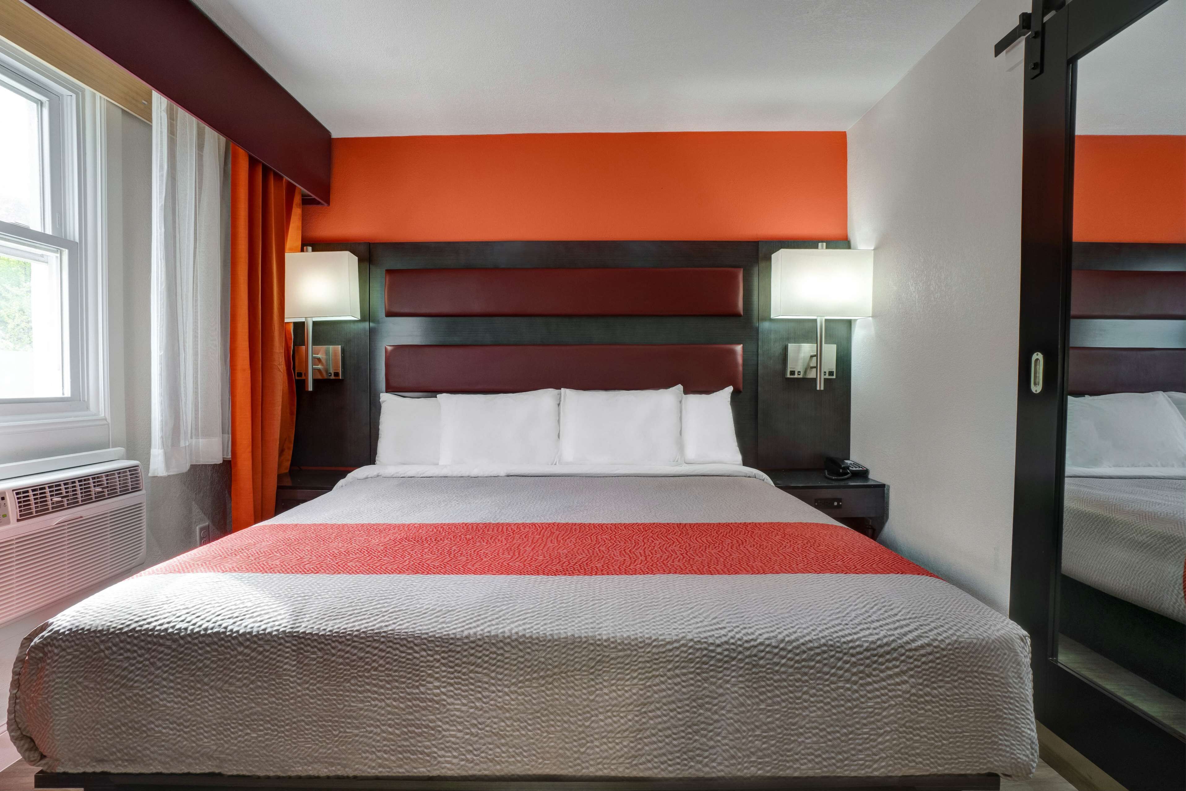 Une chambre d’hôtel avec un grand lit, deux tables de chevet avec des lampes, une fenêtre avec des rideaux et un radiateur fixé au mur.