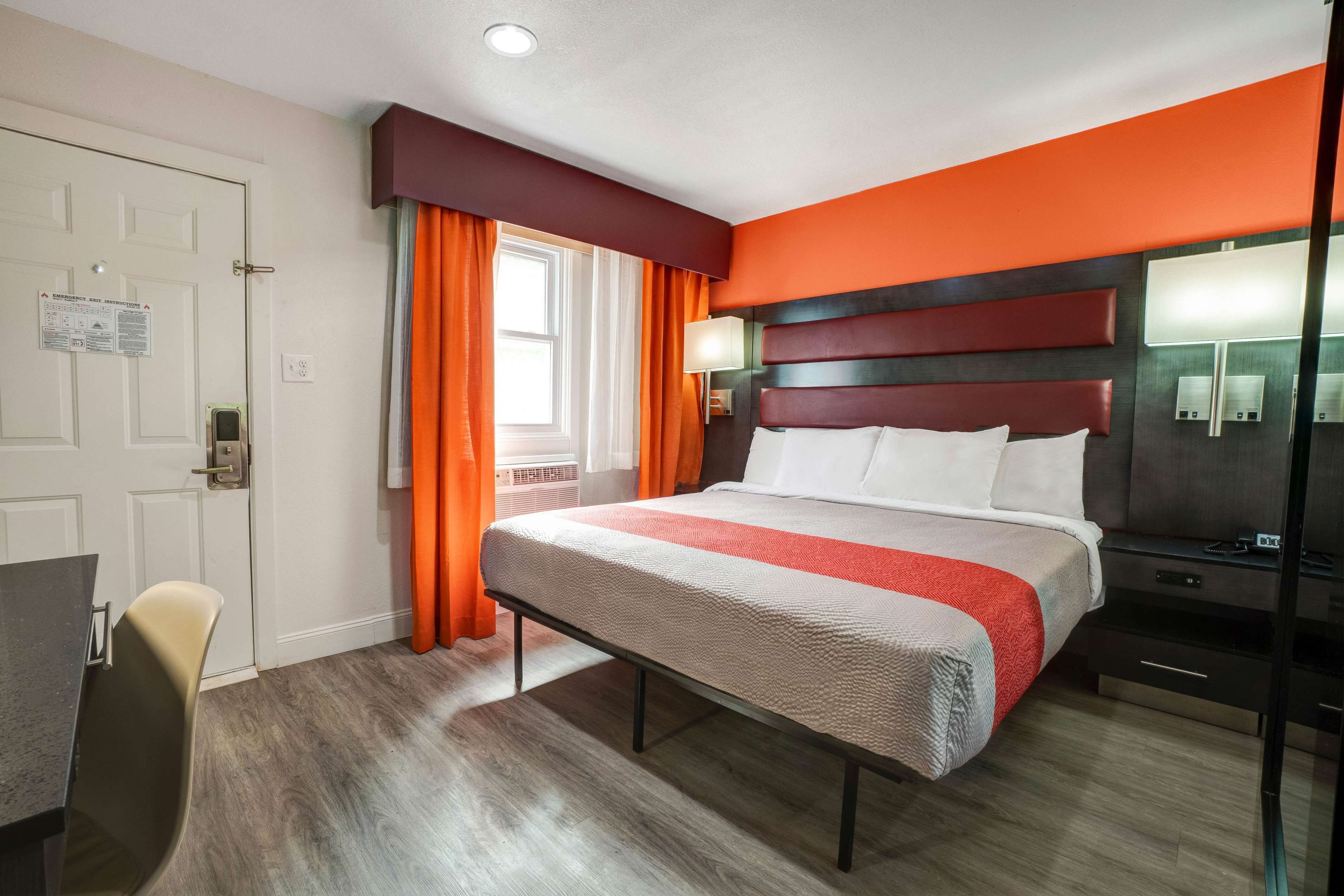 Une chambre d’hôtel avec un lit, un bureau, une chaise et une fenêtre avec des rideaux.