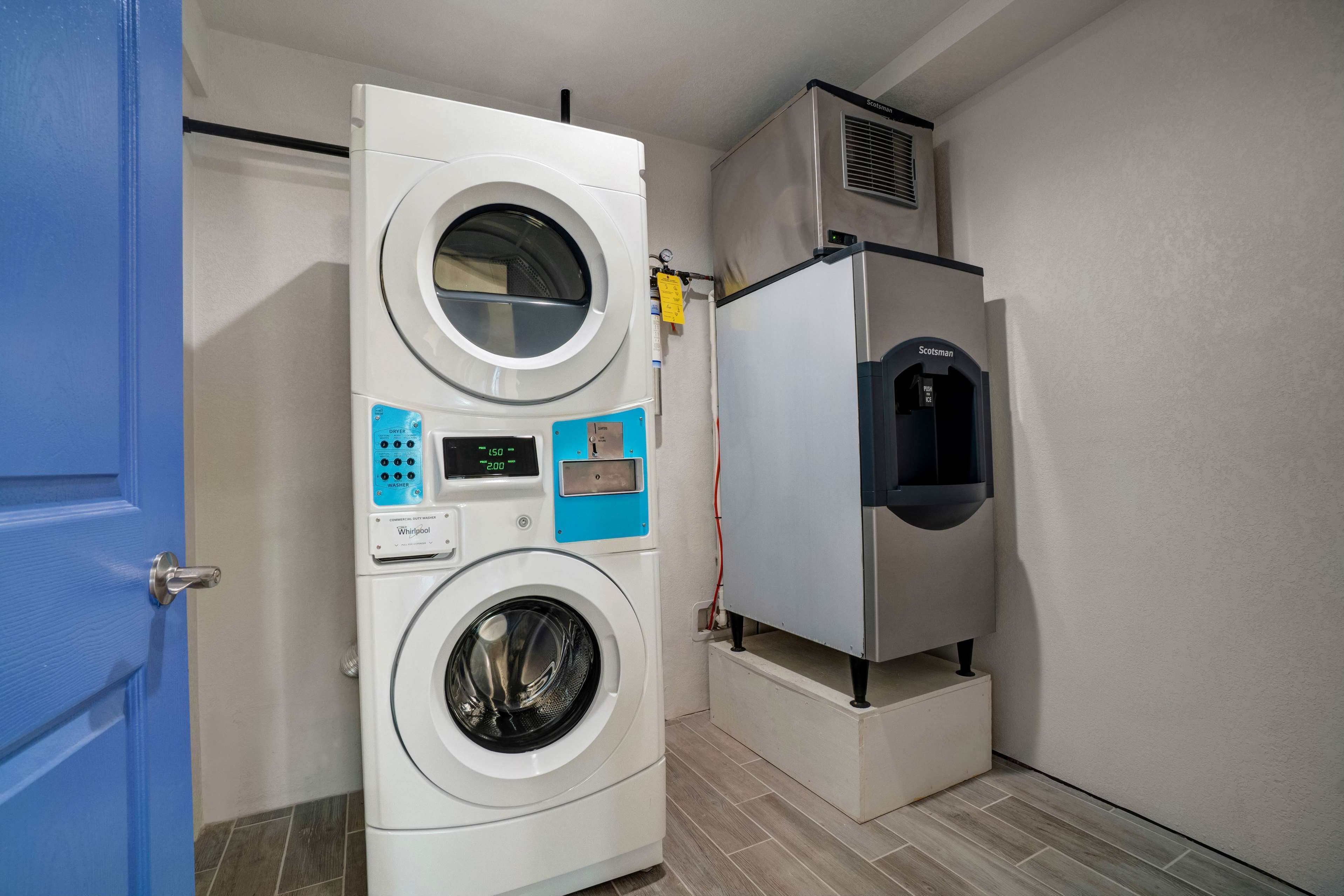A compact laundry room with a front-loading washer and dryer, a small refrigerator, and a blue door.