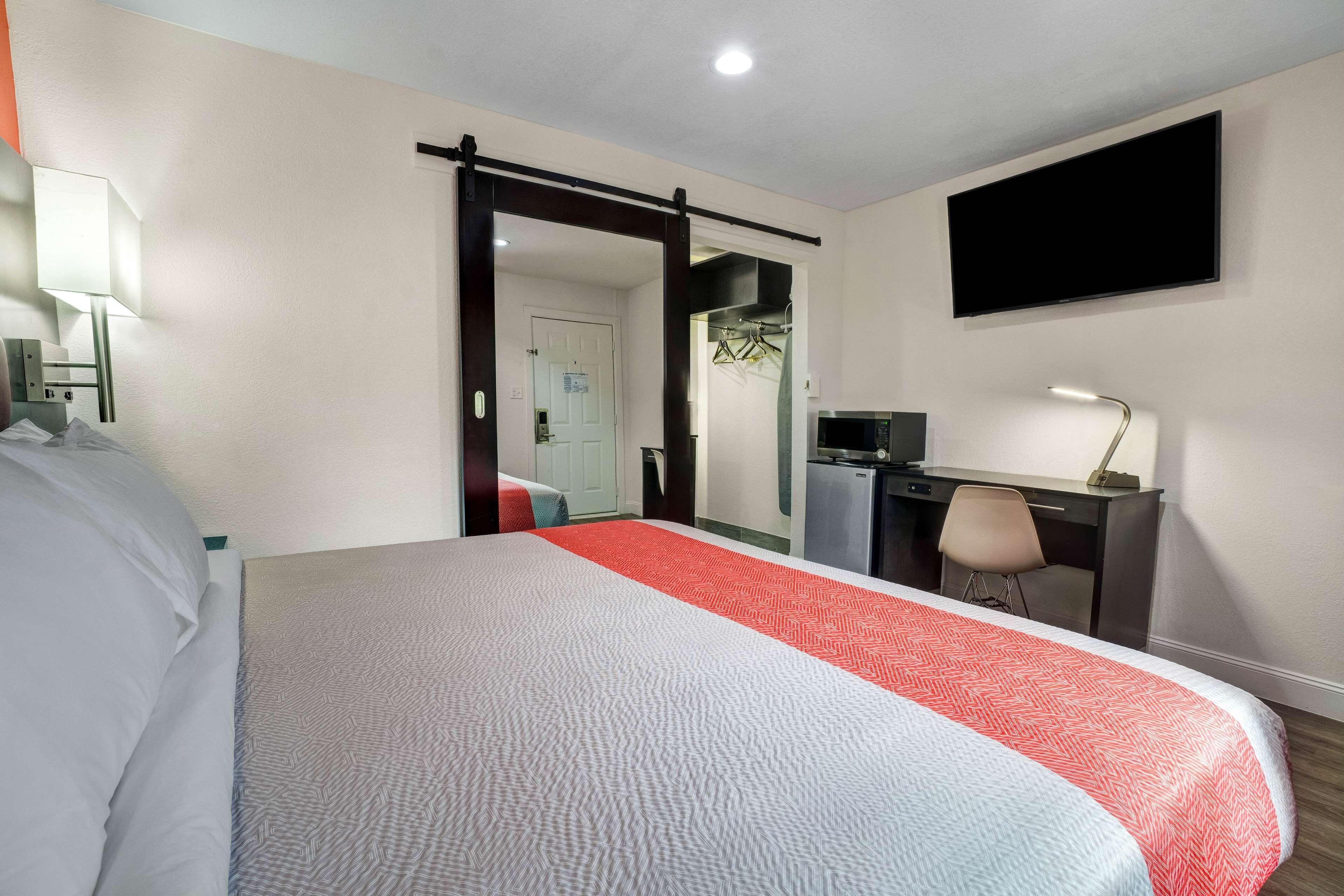 A hotel room with a bed, desk, chair, TV, and a door leading to a bathroom.