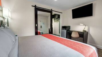 A hotel room with a bed, desk, chair, TV, and a door leading to a bathroom.
