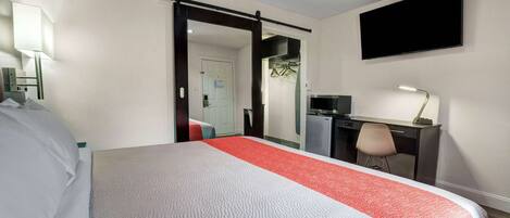 A hotel room with a bed, desk, chair, TV, and a door leading to a bathroom.