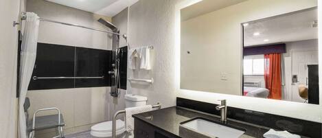 A modern bathroom with a glass shower enclosure, a white toilet, a sink with a black countertop, and a large mirror.