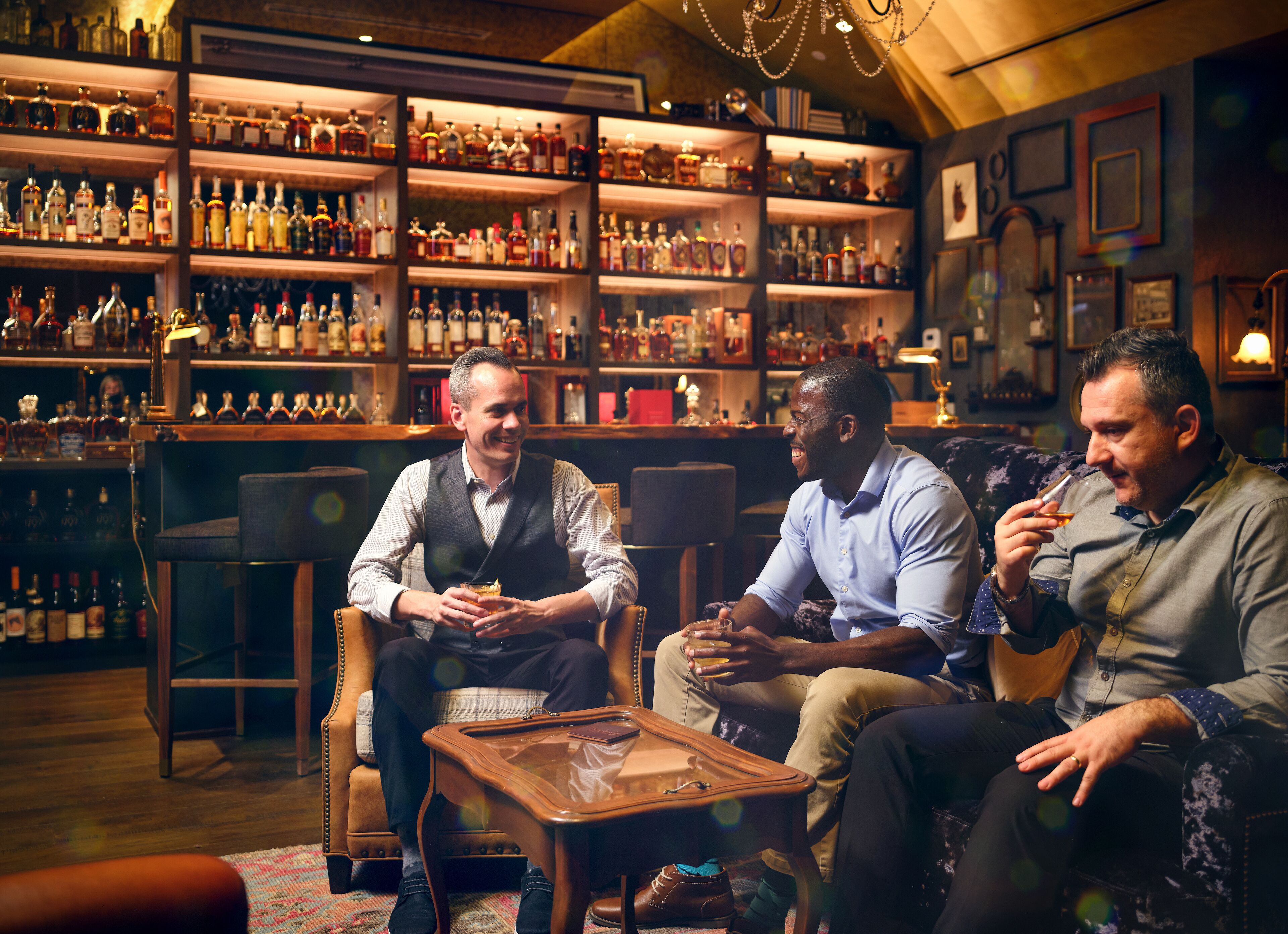 A bar area with shelves of liquor bottles, leather seating, and a wooden coffee table.