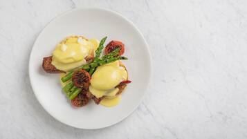 Une assiette de nourriture comprenant des œufs Bénédicte, des asperges et des tomates grillées, le tout présenté sur une assiette blanche.
