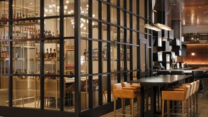 A modern bar area with glass partitions, bar stools, and a variety of bottles. - Louisville Marriott Downtown (Louisville)