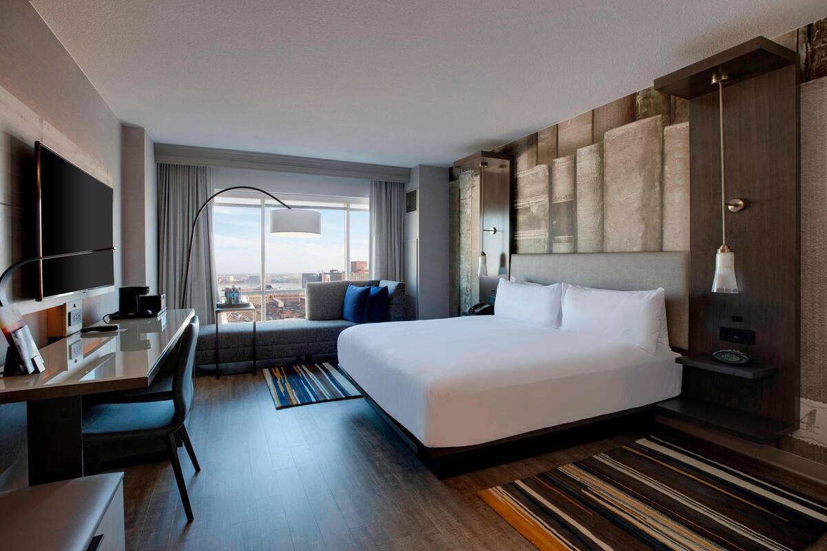Ein modernes Hotelzimmer mit einem großen Bett, einem Schreibtisch, einem Fernseher und Blick auf die Stadt.