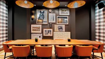 A conference room with a large wooden table, orange chairs, and pendant lighting.