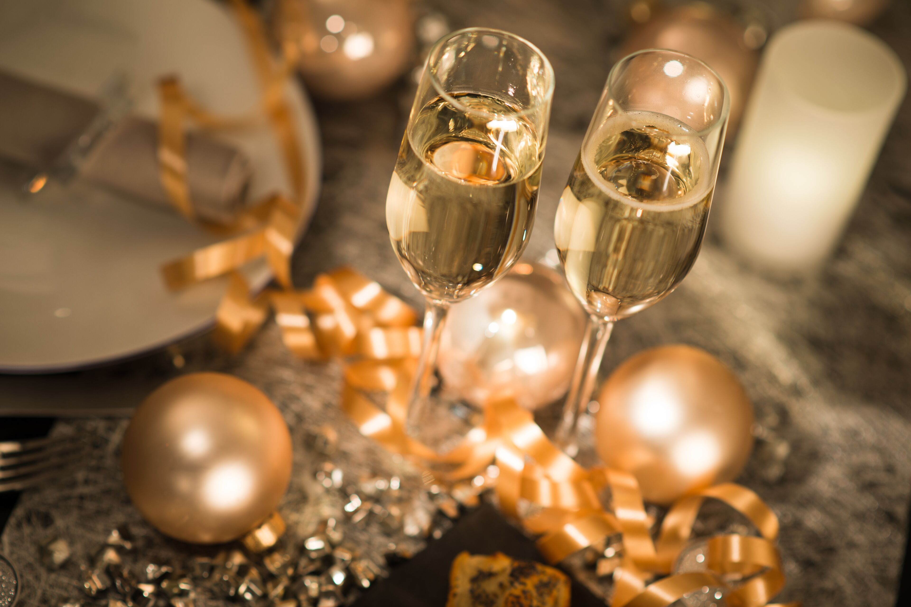 Two champagne flutes on a table with gold ribbons and ornaments.