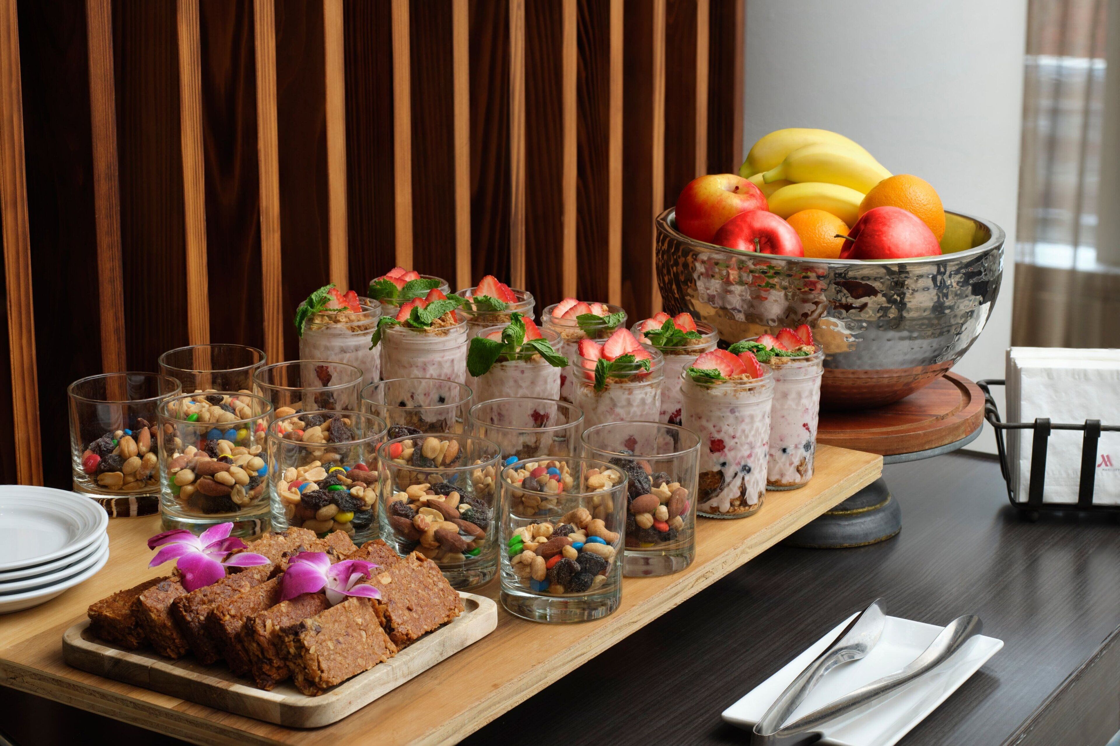 A buffet table with various food items, including jars of dessert, a bowl of fruit, and a tray of brownies.